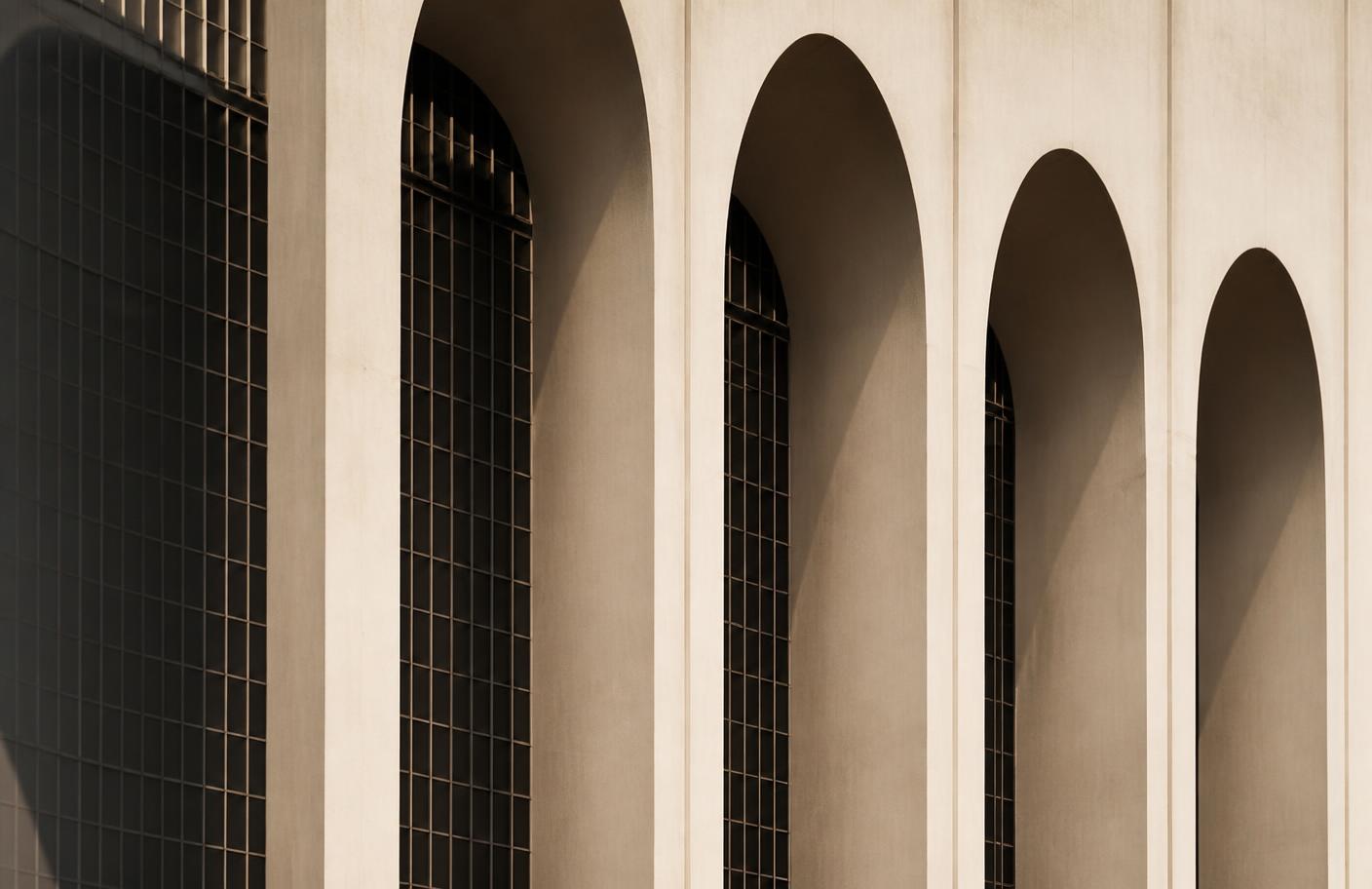 Repeating concrete arches with fine steel window grids casting geometric shadows